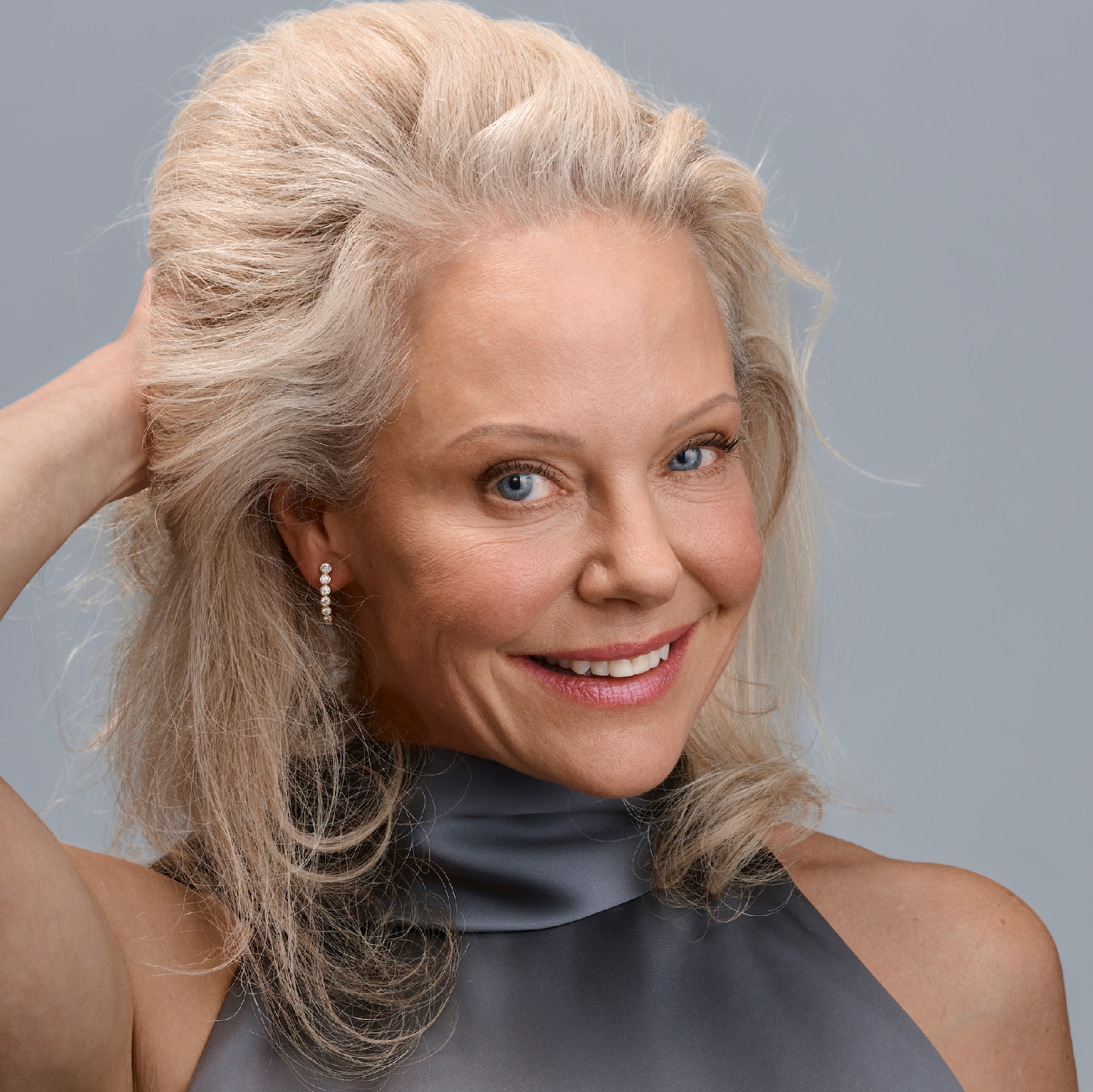 Woman with gray hair touching her hair against a gray background