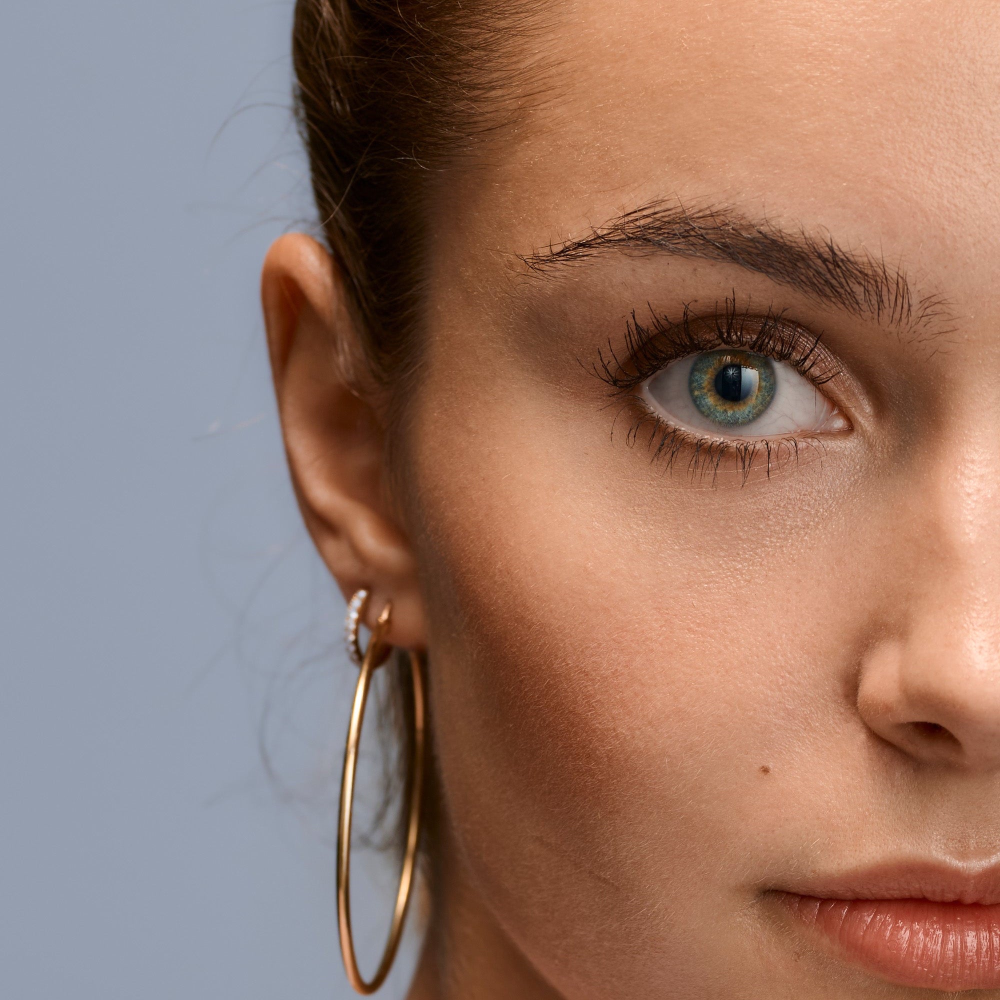 Close-up of a woman wearing gold hoop earrings against a gray background